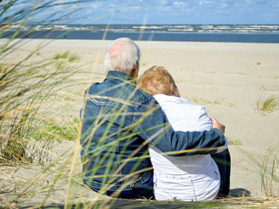 Ein älteres Paar sitzt am Strand und blickt auf das Meer.