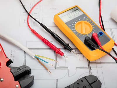 Ein Multimeter liegt auf einem technischen Plan, umgeben von Kabeln und Prüfspitzen.