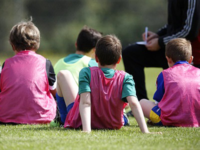 Vier Kinder in pinken Trainingswesten sitzen auf einem Fußballfeld.